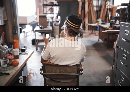 Rear view of carpenter using smart phone in workshop Stock Photo