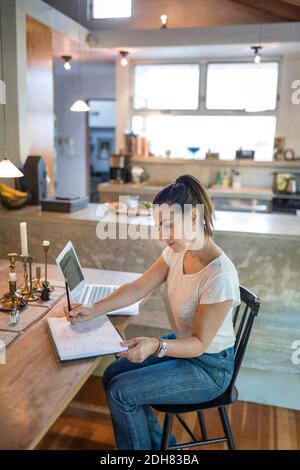 Woman Using Computer Work Person working on a laptop at a dining table in a home setting, using a ...