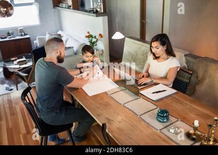 Mother working on laptop while father assisting son in doing homework at dining table Stock Photo
