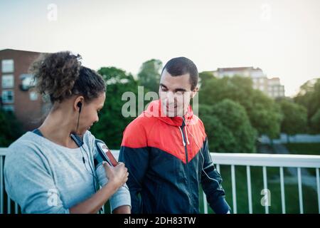 Man looking at woman using smart phone armband while walking at sidewalk Stock Photo