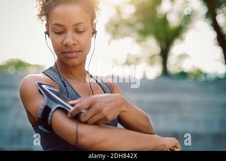 Woman using smart phone armband while standing at park Stock Photo