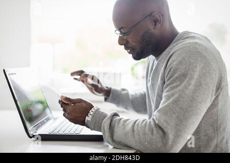 Side view of man using smart phone with laptop at table Stock Photo