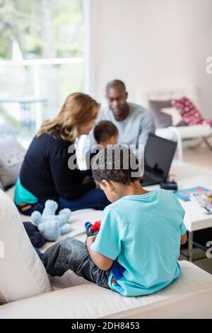 Rear view of boy playing on sofa with family in background Stock Photo