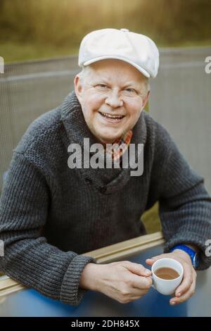 Portrait of happy man holding coffee cup while sitting at table outdoors Stock Photo
