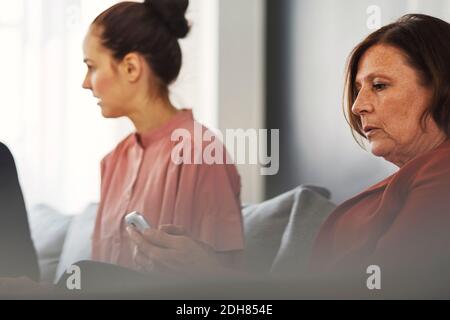 Mature businesswoman using mobile phone while sitting by colleague in office Stock Photo