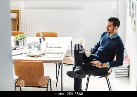 Mid adult businessman having coffee at desk in office Stock Photo