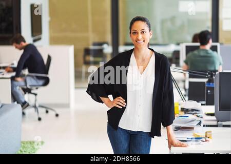 Portrait of happy young businesswoman with male colleagues working in background at office Stock Photo