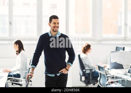 Happy mid adult businessman with colleagues working in background at office Stock Photo