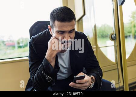 Young man text messaging through mobile phone in tram Stock Photo
