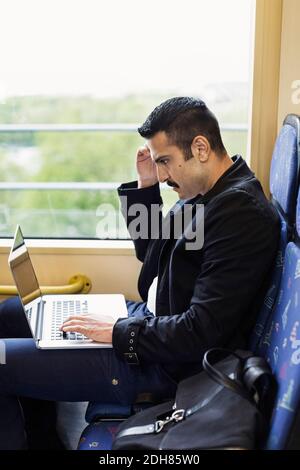 Side view of young man using laptop in tram Stock Photo