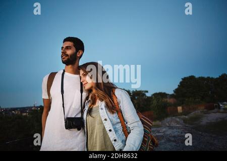 Thoughtful tourist couple looking away while standing against clear blue sky Stock Photo