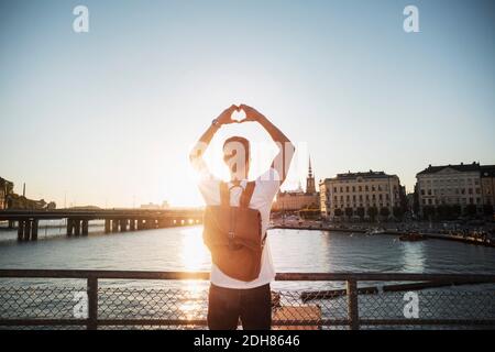 Male tourist making heart shape with hands in city against clear sky Stock Photo