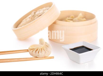 chopsticks holding a chinese dumpling, soy sauce and bamboo basket in white background Stock Photo