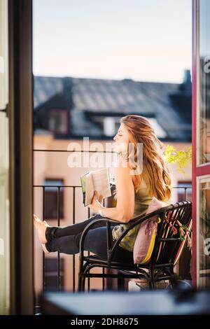 Side view of woman looking away while holding guidebook at balcony Stock Photo