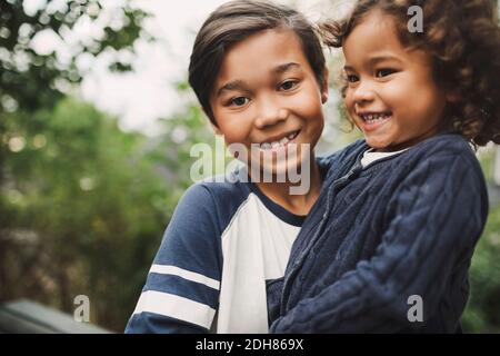 Portrait of happy boy carrying sister at yard Stock Photo