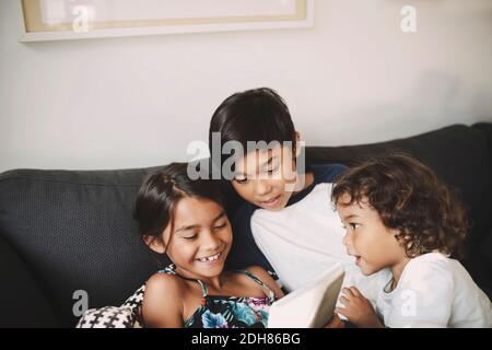 Siblings using digital tablet on sofa at home Stock Photo