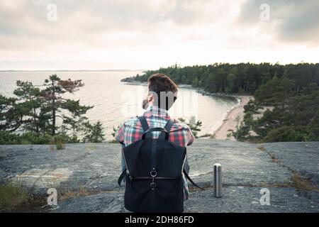 Rear view of wonderlust man sitting on rock at lakeshore Stock Photo