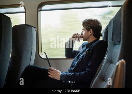 Side view of thoughtful businessman holding digital tablet in train Stock Photo