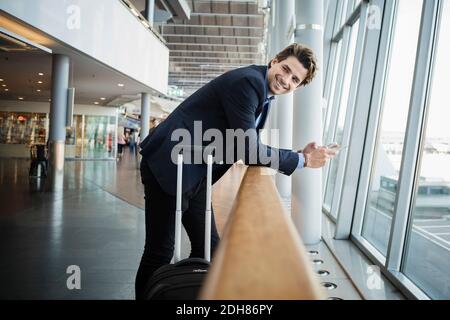 Side view of happy businessman leaning on railing at airport Stock Photo