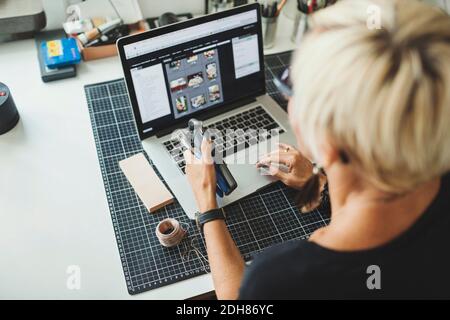 High angle view of industrial designer using laptop while holding product at home office Stock Photo