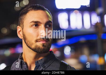 Thoughtful young man looking away in city at night Stock Photo