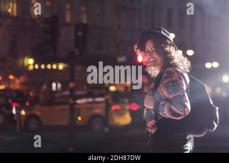 Side view portrait of smiling woman standing on city street at night Stock Photo