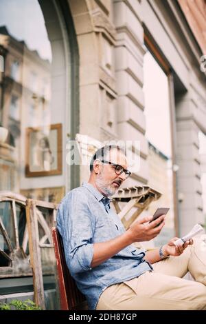 Man using mobile phone while sitting outside shop Stock Photo