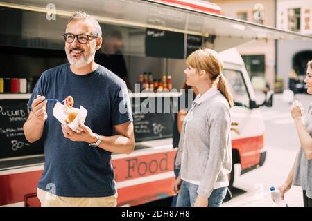Mature man eating food while standing against truck at street Stock Photo