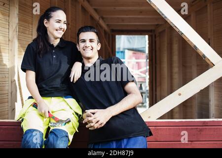 Portrait of happy carpentry student with female friend sitting on wooden cabin Stock Photo