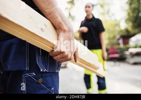 Midsection of male student carrying wooden planks with classmate standing in background Stock Photo