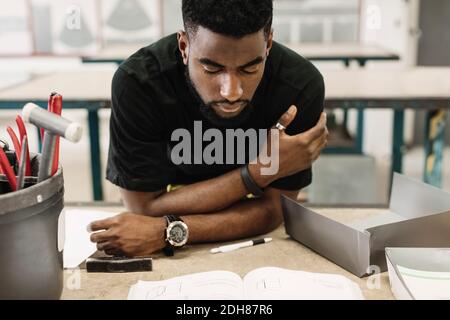 Young male high school student reading book in workshop Stock Photo