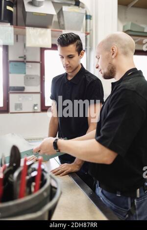 Teacher assisting male trainee over project in workshop Stock Photo