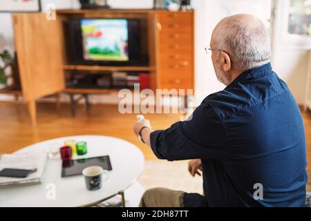 Rear view of senior man changing channels at home Stock Photo