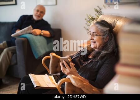 Happy senior woman using mobile phone while man sitting on sofa at home Stock Photo