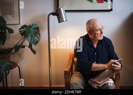 Senior man looking away while holding smart phone at home Stock Photo