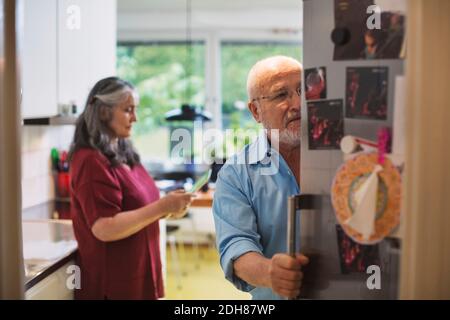 Senior man opening refrigerator while woman using digital tablet at home Stock Photo
