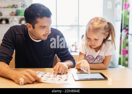 Mid adult male teacher looking at girl using digital tablet at preschool Stock Photo