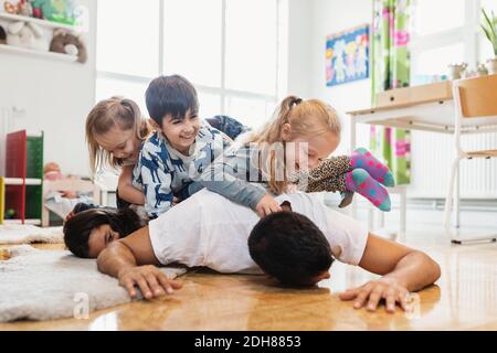 Happy children lying on top of teacher at preschool Stock Photo