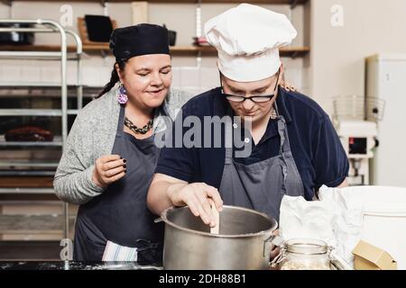 Mature baker helping coworker in cooking at commercial kitchen Stock Photo