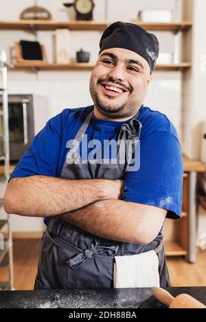 Smiling man with arms crossed standing in kitchen Stock Photo