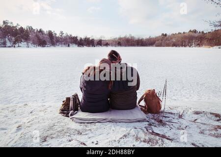 Rear view of male and female hiker sitting on snow covered field Stock Photo