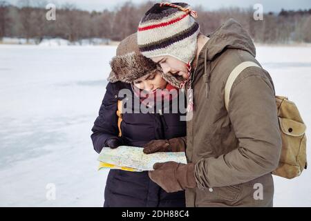 Couple looking at map while standing on field during winter Stock Photo