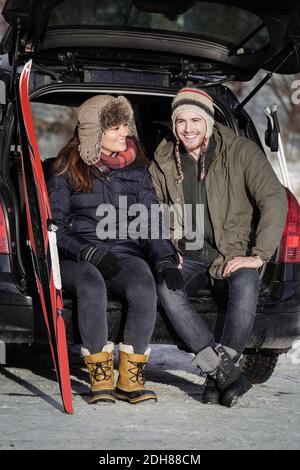 Happy couple talking while sitting on car trunk Stock Photo