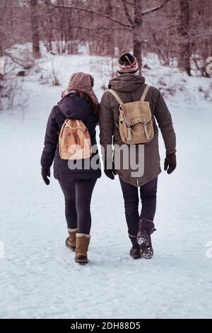 Full length rear view of couple walking on snow covered field Stock Photo