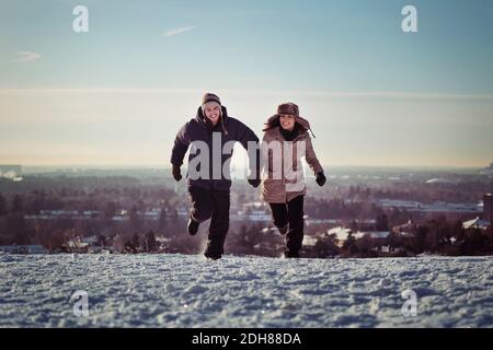 Full length of happy couple running on snow covered mountains Stock Photo