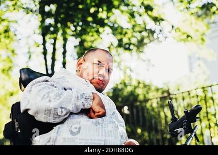 Low angle view of disabled man on wheelchair against trees Stock Photo