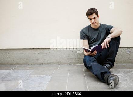 Young man sitting on floor reading a book Stock Photo