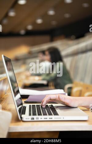 Close-up of human hand typing on laptop keyboard with people in background in auditorium Stock Photo