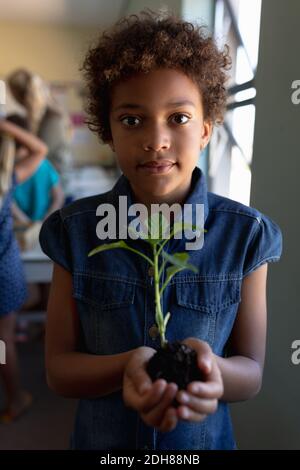 Schoolgirl standing holding a seedling plant in a jar of earth in an elementary school classroom Stock Photo