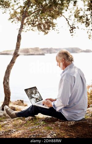 Senior man using laptop outdoors on picnic Stock Photo